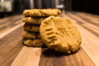 Stack of Peanut Butter Cookies with crosshatch fork marks, one leaning cookie in front on wood