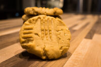 A Peanut Butter Cookie with crosshatch fork marks stands in front of stacked cookies on a wooden table.