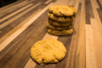 Stack of Peanut Butter Cookies with crosshatch fork marks, one cookie set apart on a striped wooden table.