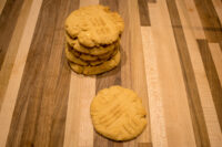 Stack of Peanut Butter Cookies with fork-tine crosshatch marks, one cookie set beside the stack on a wooden board.