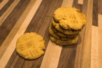 A stack of Peanut Butter Cookies with fork crosshatch marks beside one single cookie on a striped wood surface.
