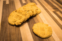 Five crosshatch-topped Peanut Butter Cookies with peanut flecks on a striped wooden board