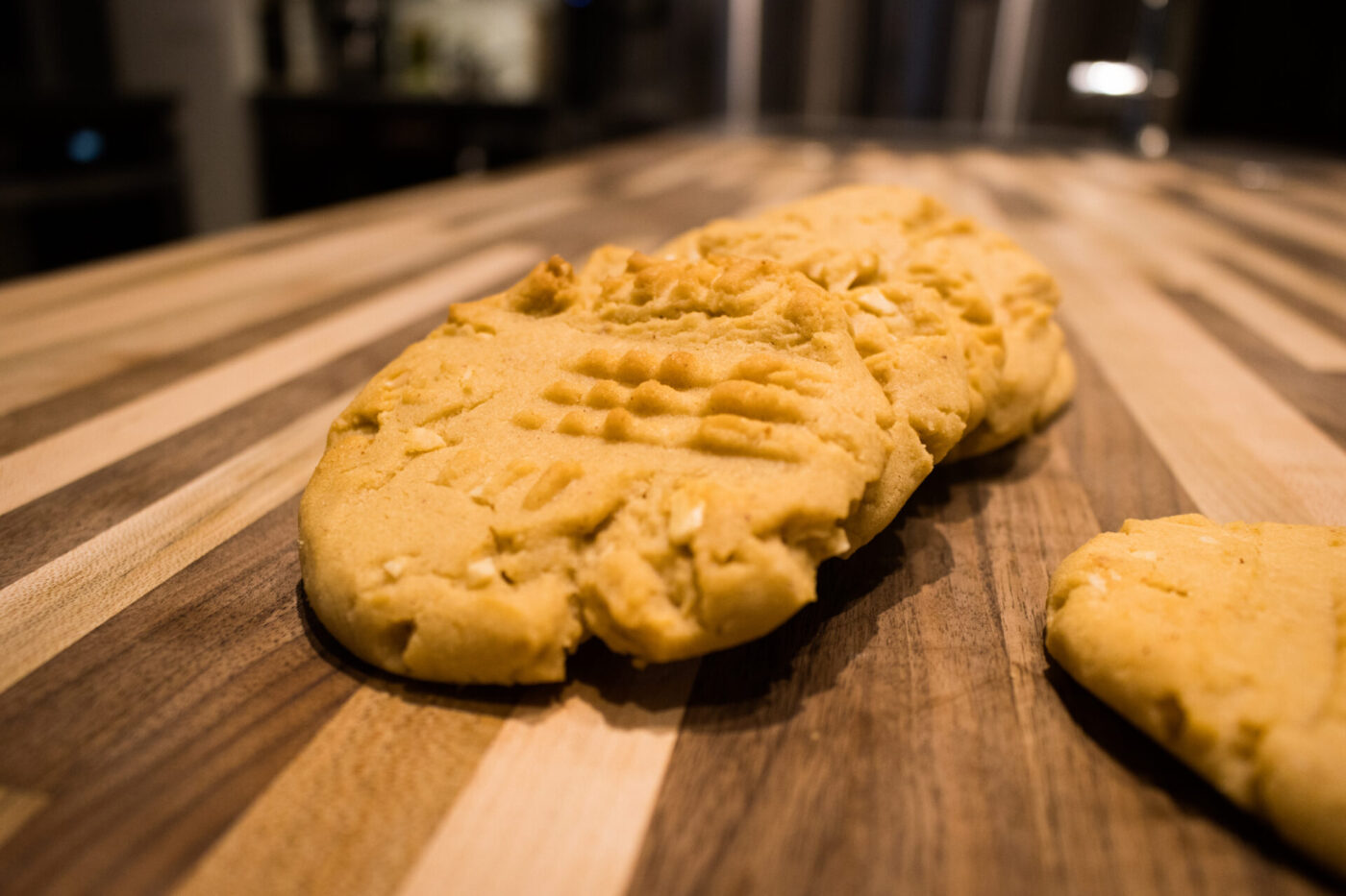 A Peanut Butter Cookies with crosshatch fork marks and peanut flecks on a striped wooden board.