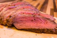 Sliced Beef Picanha in Salt Crust, showing pink medium-rare interior and dark seasoned crust on a wooden board