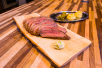 Sliced Beef Picanha fanned on a wooden board with a herb butter dollop, mashed potato and greens plated behind