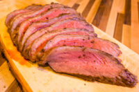 Sliced Beef Picanha in Salt Crust fanned on a wooden board, pink center and dark crusted edge.