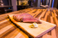 Sliced Beef Picanha in Salt Crust fanned on a wooden board with a dollop of herb butter.