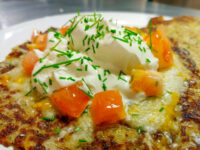 Golden Potato Pancakes Bramboraky topped with sour cream, diced tomato, and chives on a white plate.