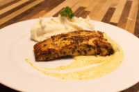 Seared Salmon in Mustard Sauce with a blackened crust, mashed potato, and pale cream sauce on a white plate.