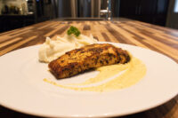 Seared Salmon in Mustard Sauce fillet with pale sauce swirl, mashed potato, and herb garnish on a white plate.