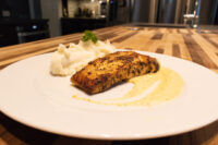 Seared salmon in mustard sauce on a white plate with piped mashed potato and herb garnish