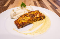 Seared fillet of Salmon in Mustard Sauce beside mashed potatoes and a parsley sprig on a white plate.