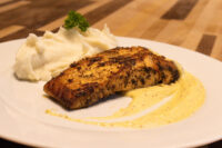 Seared Salmon in Mustard Sauce fillet with mashed potatoes and pale cream sauce on a white plate