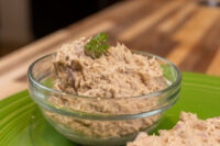 Glass bowl of Sardines Dip or Spread garnished with parsley, on a green plate with bread