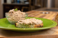 Sardines Dip or Spread piled on toasted bread, with more in a glass bowl on a green plate.