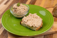 Sardines Dip or Spread on toasted bread beside a glass bowl of the same mixture on a green plate