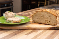 Bowl of Sardines Dip or Spread with herb garnish and a topped bread slice on a green plate beside a sliced loaf.