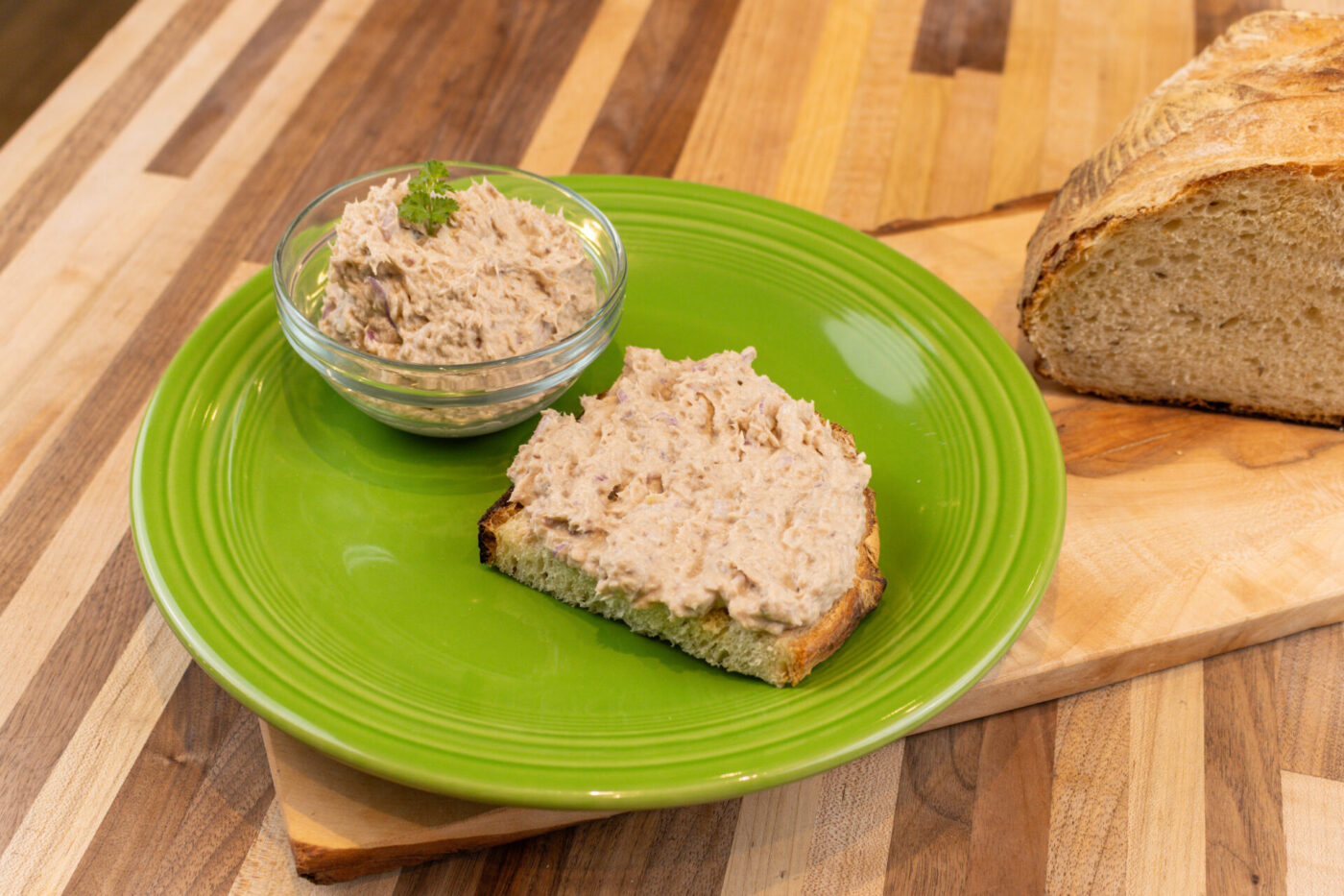 Glass bowl of Sardines Dip or Spread beside a slice of bread spread with it on a green plate.