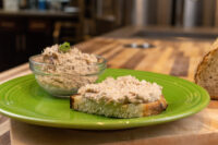 Sardines Dip or Spread in a glass bowl beside a toasted slice spread with the same mixture on a green plate