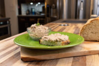 Sardines Dip or Spread on a slice of toasted bread beside a glass bowl of the same spread on a green plate
