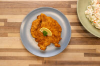 Chicken Schnitzel Golden breaded Chicken Schnitzel on a grey plate with lemon wedge and parsley garnish