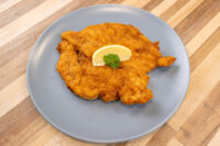 Chicken Schnitzel Golden breaded Chicken Schnitzel on a gray plate, garnished with a lemon slice and parsley.