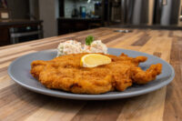 Chicken Schnitzel Golden fried Chicken Schnitzel on a gray plate with a lemon wedge, herb sprig, and coleslaw