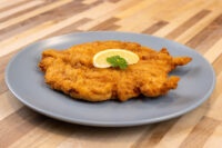 Chicken Schnitzel Golden fried Chicken Schnitzel on a grey plate with a lemon wedge and parsley, on a wooden table.