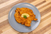 Chicken Schnitzel Golden fried Chicken Schnitzel on a grey plate with parsley and lemon wedge on wood table.