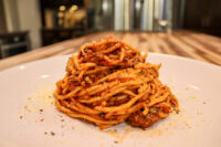 Spaghetti Bolognese Twirled mound of Spaghetti Bolognese with meat sauce and grated cheese on a white plate.