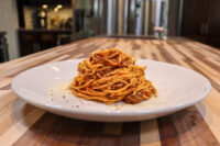 Spaghetti Bolognese Twirled spaghetti bolognese topped with grated parmesan on a white plate atop a wooden table