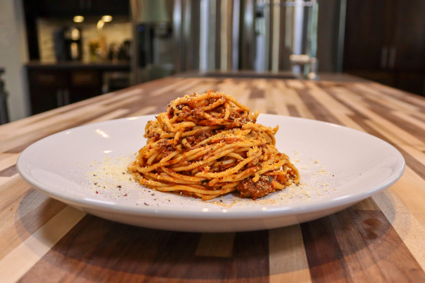 Spaghetti Bolognese Twirled Spaghetti Bolognese topped with grated parmesan and herbs on a white plate.