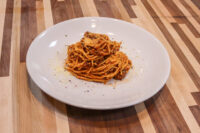 Spaghetti Bolognese A mound of Spaghetti Bolognese with red meat sauce and herb garnish on a white plate.