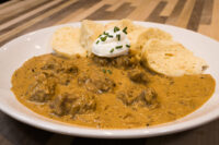 Bowl of Szegedin Goulash with sour cream and chives, served with bread on a white plate