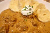 Bowl of Szegedin Goulash with sour cream and chives, served alongside sliced dumplings.