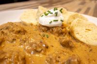 Bowl of Szegedin Goulash with creamy paprika sauce, sour cream dollop, chives, and bread slices.