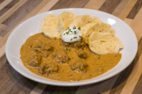 Bowl of Szegedin Goulash with tender meat in creamy paprika sauce, sour cream, chives, and bread slices.