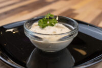 Glass bowl of Czech Tartar Sauce Tatarka with a parsley sprig on a black plate
