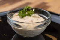 Glass bowl of creamy Czech Tartar Sauce Tatarka garnished with a fresh herb sprig on a dark surface.