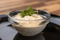 Glass bowl of Czech Tartar Sauce Tatarka garnished with a parsley sprig, set on a dark plate.