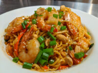 Plate of Thai Noodles with Shrimp topped with peanuts, sliced chili, scallions, and sesame seeds.