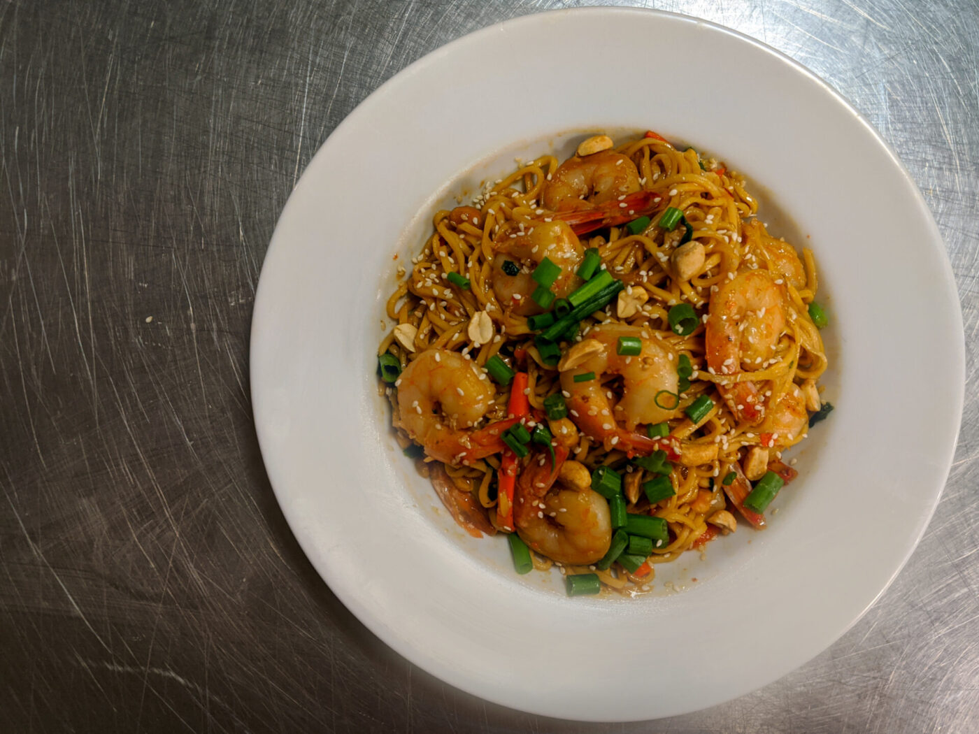 Overhead shot of Thai Noodles with Shrimp topped with scallions, peanuts, and sesame seeds in a white bowl.