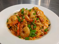 White bowl of Thai Noodles with Shrimp topped with peanuts, green onions, and sesame seeds.