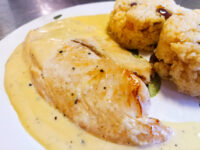 Tilapia in a Creamy Wine Sauce Pan-seared tilapia fillet in creamy wine sauce, served with two mounds of studded couscous on a floral white plate.