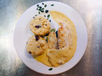 Tilapia in a Creamy Wine Sauce Tilapia in a Creamy Wine Sauce with pale cream sauce, herb flakes, and two grain cakes on a white plate.