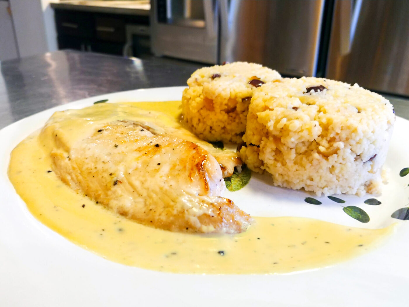 Tilapia in a Creamy Wine Sauce Pan-seared Tilapia in a Creamy Wine Sauce plated with couscous on a leaf-patterned white plate.