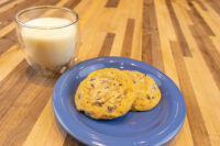 Two Chocolate Chip Cookies on a blue plate beside a glass of milk on a wood table