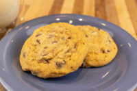 Two Chocolate Chip Cookies on a blue plate with a glass of milk behind them.