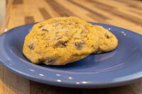 Two golden Chocolate Chip Cookies with visible chips, resting on a blue plate atop a wooden table.