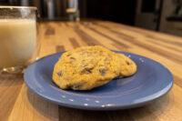 A Chocolate Chip Cookies cookie on a blue plate with a glass of milk on a wooden counter